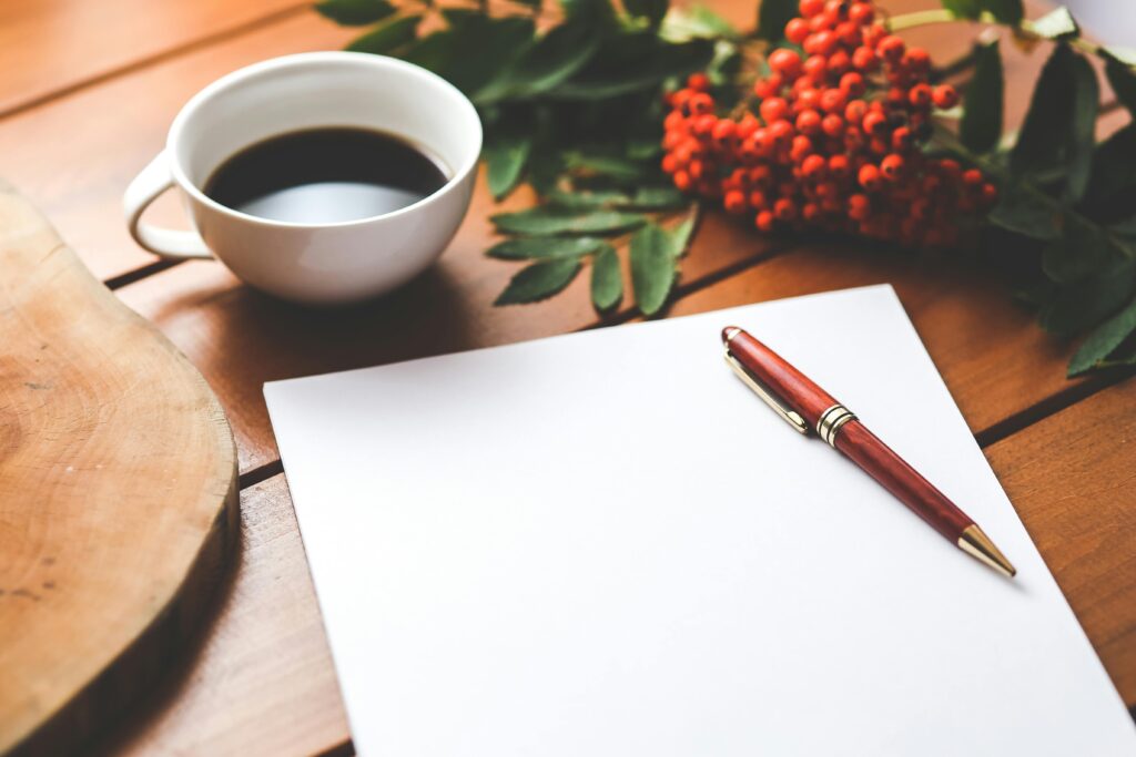 Empty paper sheet with pen and coffee next to red berries, ideal for design workspace concepts.