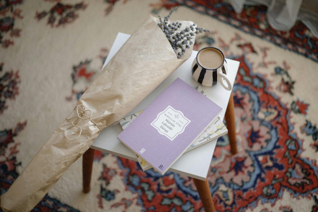 Casual table setup with a book, wrapped flowers, and coffee mug on a vintage rug.